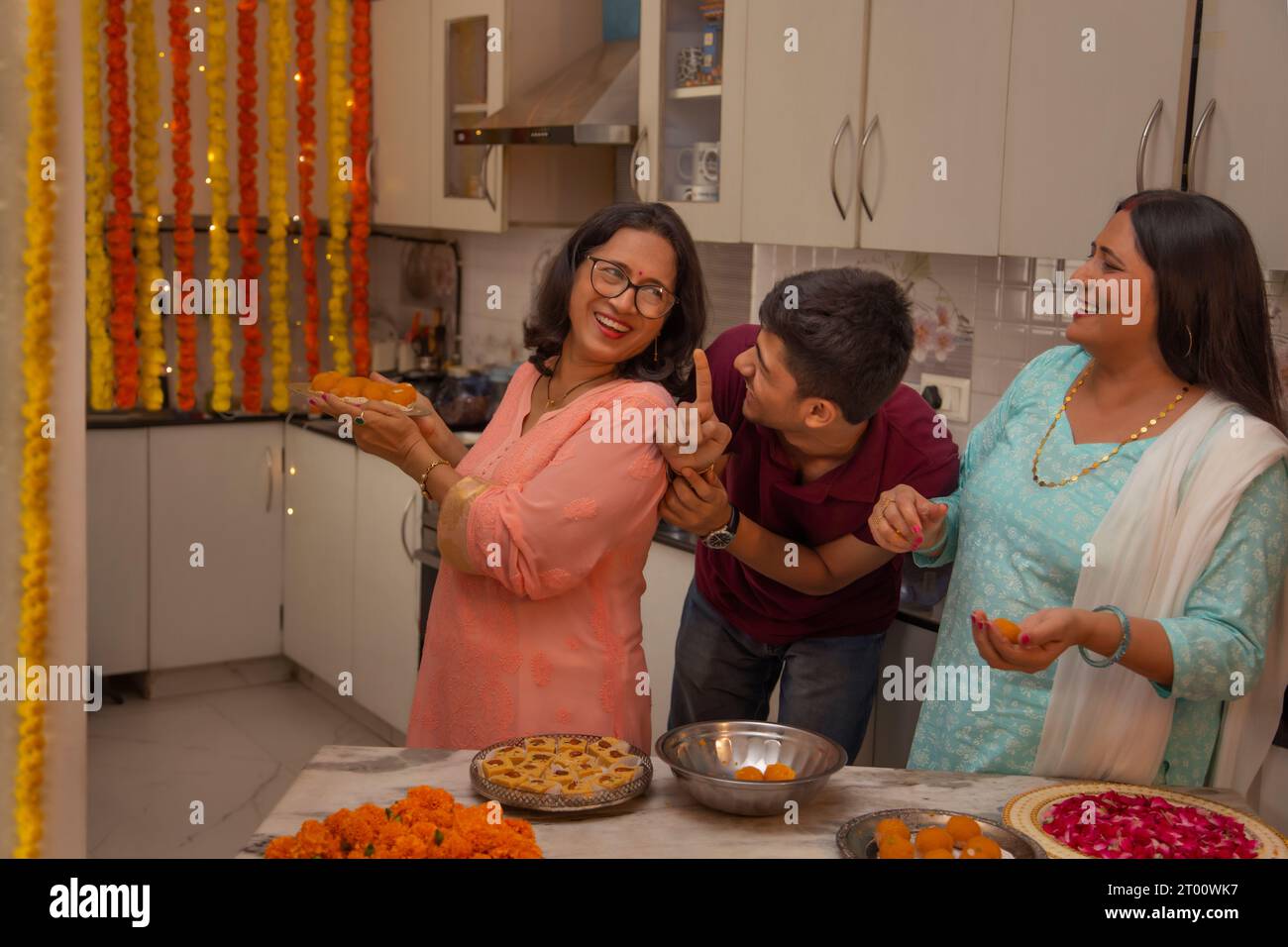 Junge, der versucht, Ladoos zu stehlen (eine traditionelle indische Süßigkeit), wie seine Mutter und Tante sie während des Festivals von Diwali machen Stockfoto