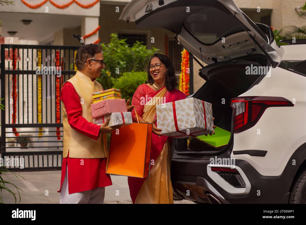 Seniorenpaar, das nach dem Einkaufen Diwali-Geschenke aus dem Kofferraum entlädt Stockfoto