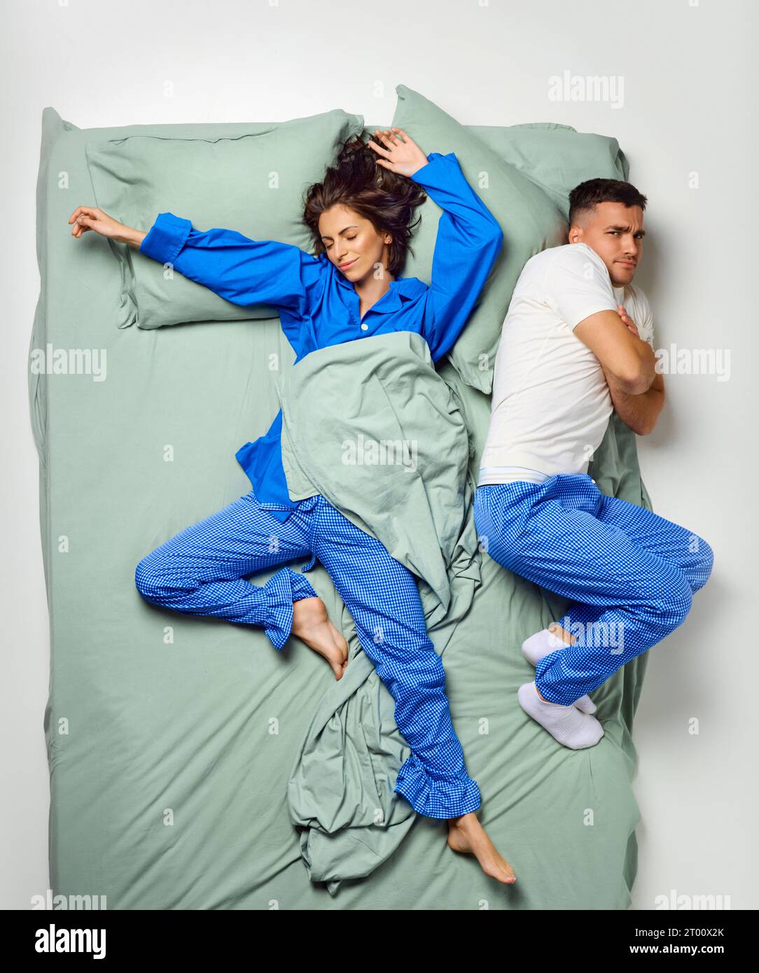 Junge, schöne Frau, bedeckt mit Decke über dem Bett und Mann, der auf der Seite lag und eiskalt im Pyjama trug, Paar, das sich in einem großen Minzbett entspannte. Stockfoto