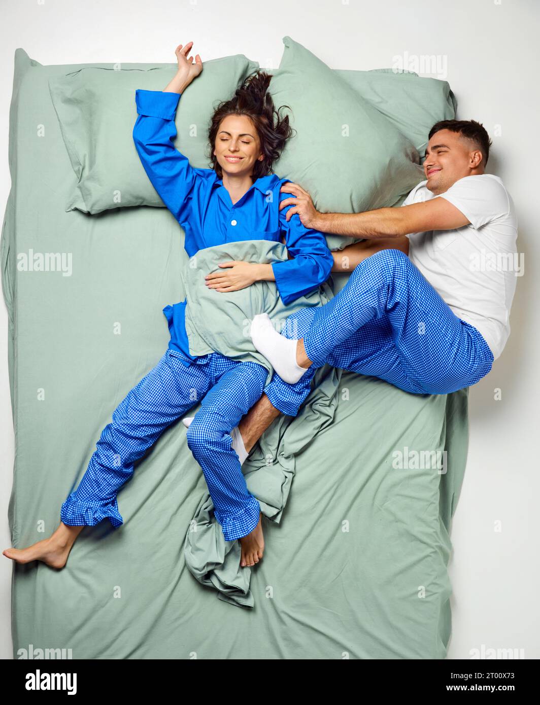 Junge, schöne Frau, bedeckt mit Decke, die über dem Bett schlief und Mann, der auf der Seite eiskalt lag, Paare, die im Pyjama tragen und sich in einem großen, mintfarbenen Bett entspannen. Stockfoto