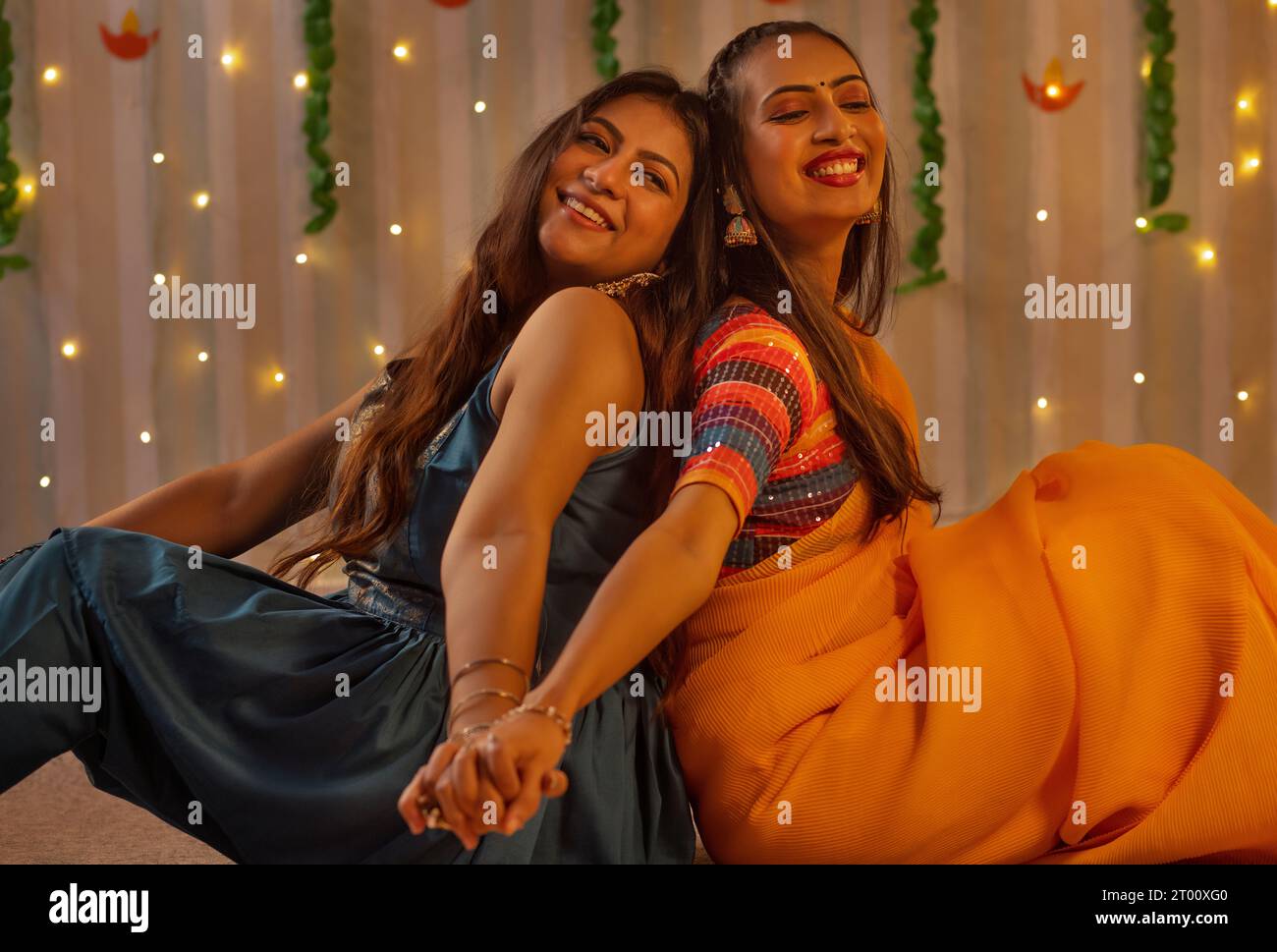 Portrait zwei fröhliche junge Frauen, die während der Diwali-Feier Rücken an Rücken sitzen Stockfoto