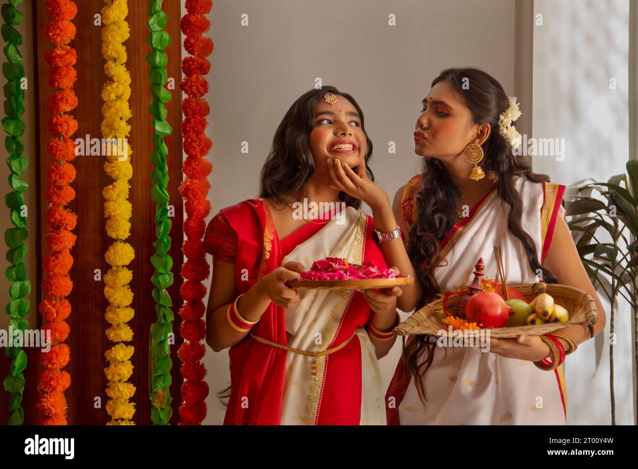 Porträt zweier bengalischer Schwester in traditionellem Outfit mit Puja Thali und Rosenblättern anlässlich von Durga Puja Stockfoto