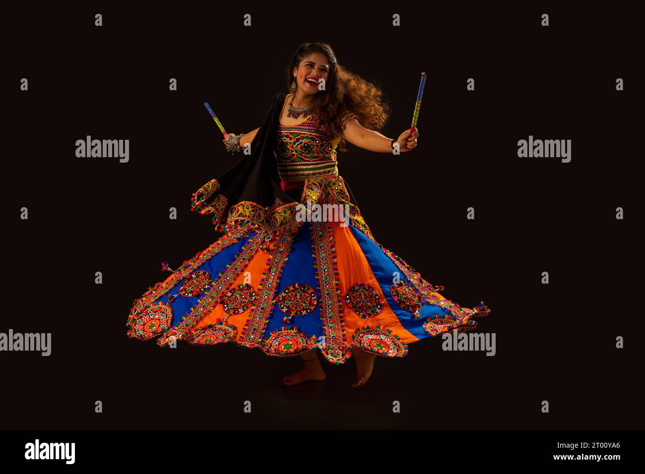 Gujarati-Frau tanzt mit Dandiya-Sticks auf einem klatschigen Hintergrund, während Navratri-Feiern Stockfoto