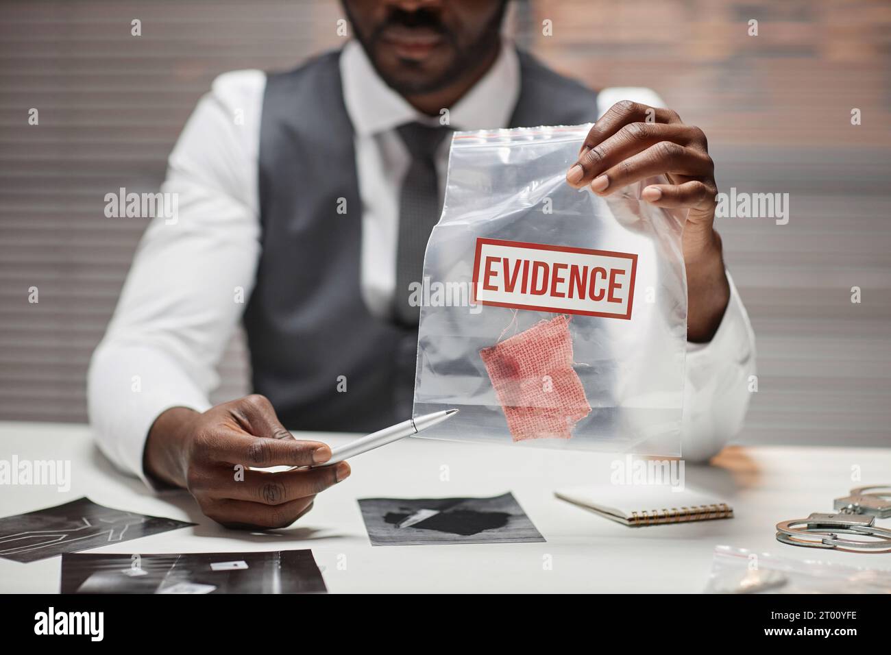 Nahaufnahme eines schwarzen männlichen Detektivs, der eine Plastiktüte mit Beweisen während des Verhörs des Verdächtigen hält, Kopierraum Stockfoto