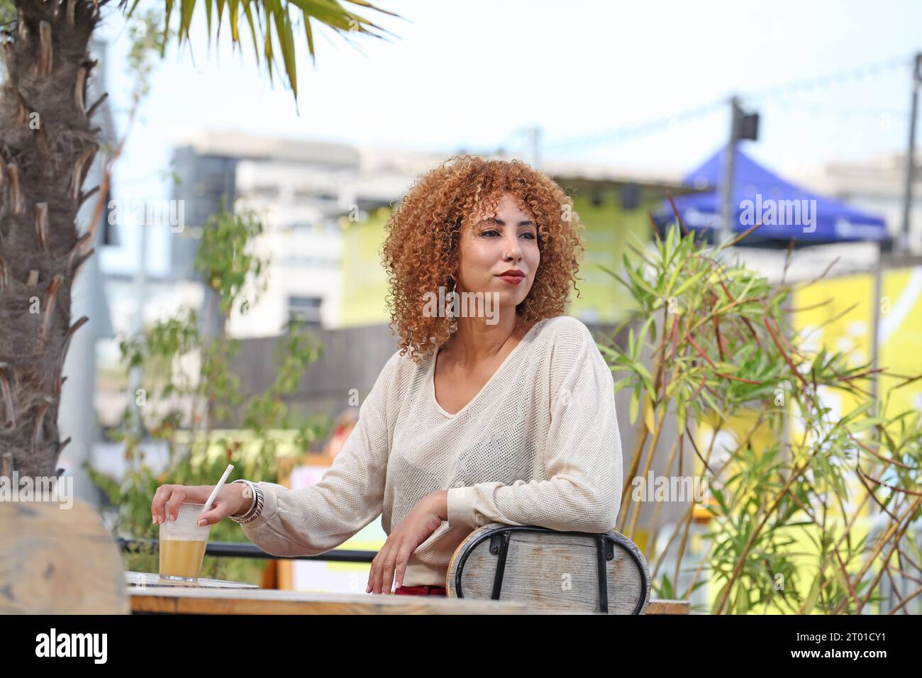 Frau mit lockigen Haaren in weißem Pullover und roter Hose, die draußen unter einem palmer-Baum in einem tropischen Land Spaß macht Stockfoto