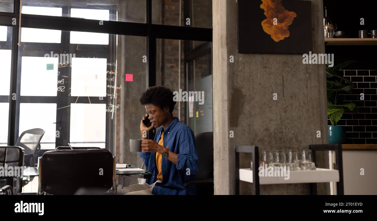 afroamerikanischer Geschäftsmann trinkt Kaffee und spricht telefonisch im Home Office, Kopierraum Stockfoto