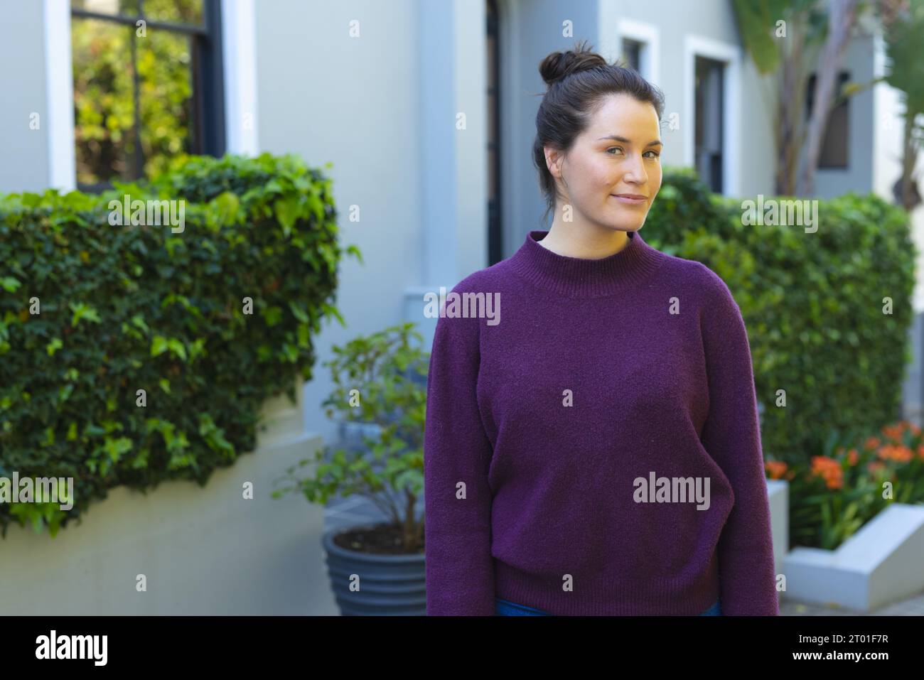 Glückliche kaukasische Frau in lila Pullover, die vor dem Haus im Garten steht Stockfoto