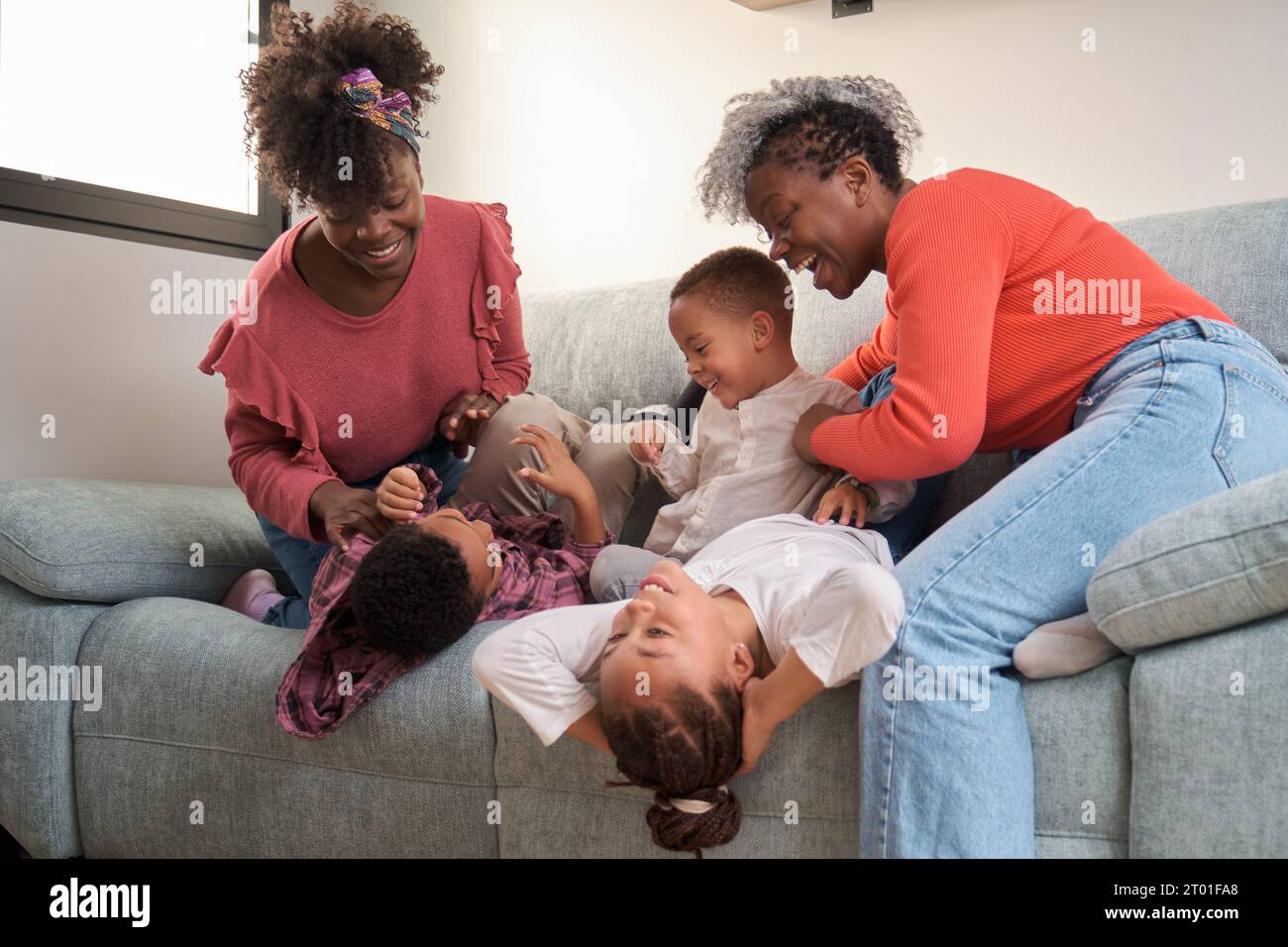 Fröhliche afrikanische Familie, die auf dem Sofa spielt, Spaß zusammen hat. Horizontale erweiterte Familie. Stockfoto