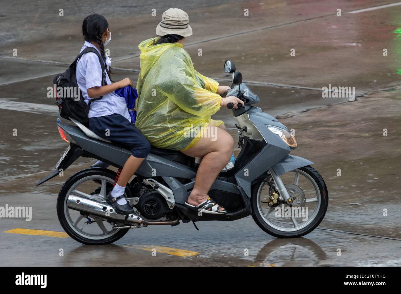 Eine Frau, die mit einem Mädchen in Schuluniform auf der regnerischen Straße in Thailand Motorrad fährt Stockfoto