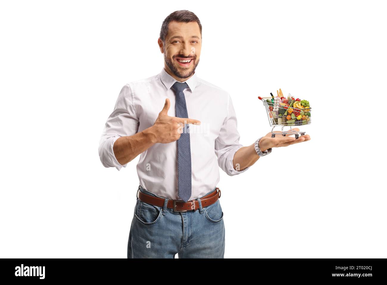 Junger lächelnder Mann, der einen Mini-Einkaufswagen mit Essen hält und isoliert auf weißem Hintergrund zeigt Stockfoto