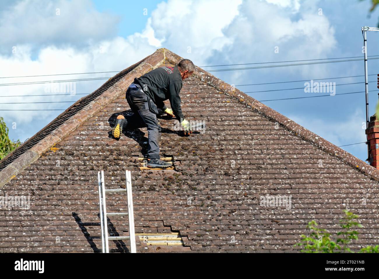 Ein Baumeister räumt ein gekacheltes Dach aus angesammeltem Schutt auf einem Vorstadthaus, Surrey England UK Stockfoto