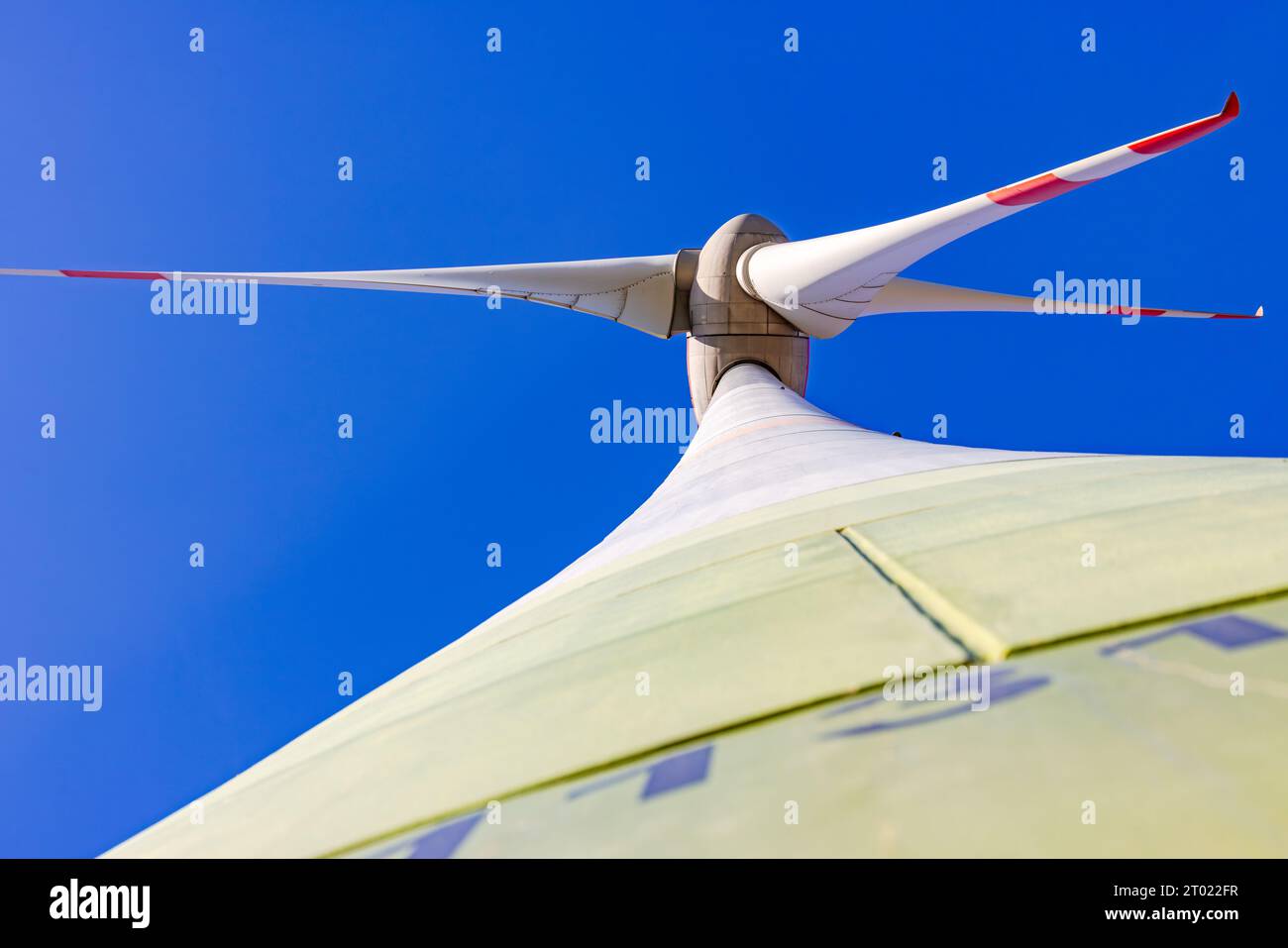 Rotor mit Maschinenhaus und Schaufeln einer Windkraftanlage mit Turm und Welle von unten vor blauem Himmel Stockfoto