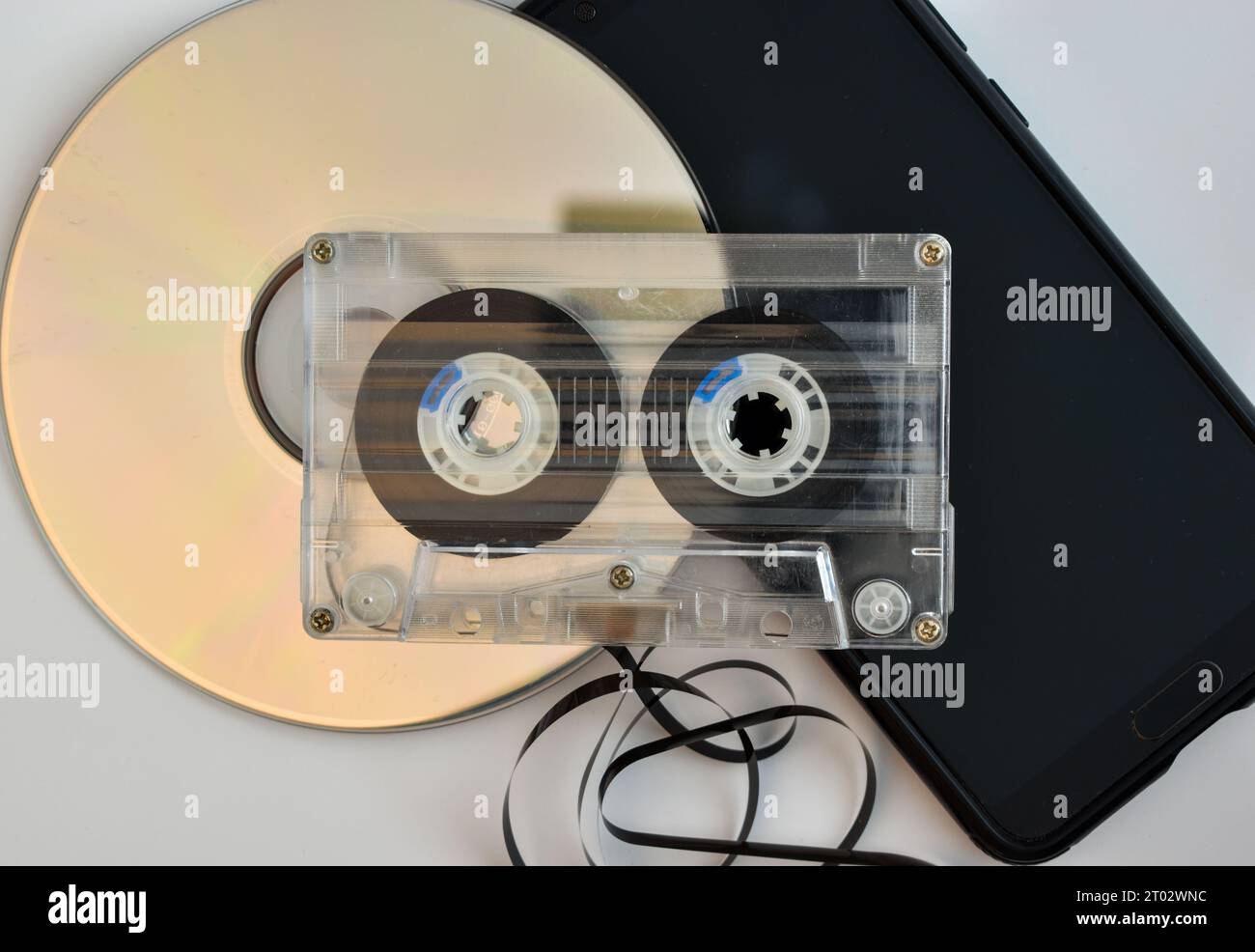 Neue und alte Transportwege für Musik, eine CD, eine Tonkassette mit teilweise entworfenen Kassetten und ein Mobiltelefon. Stockfoto