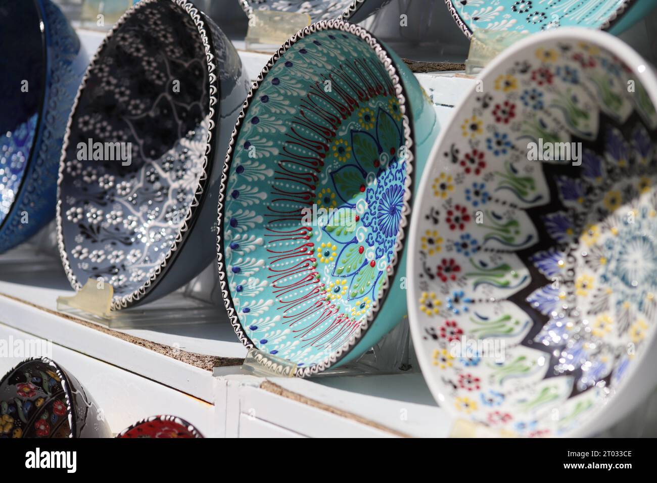 Reihen von wunderschönen, mehrfarbigen dekorativen Schalen mit verschiedenen Designs von sich wiederholenden und floralen Mustern, die auf weißen Regalen von der Seite aus gesehen ausgestellt sind Stockfoto