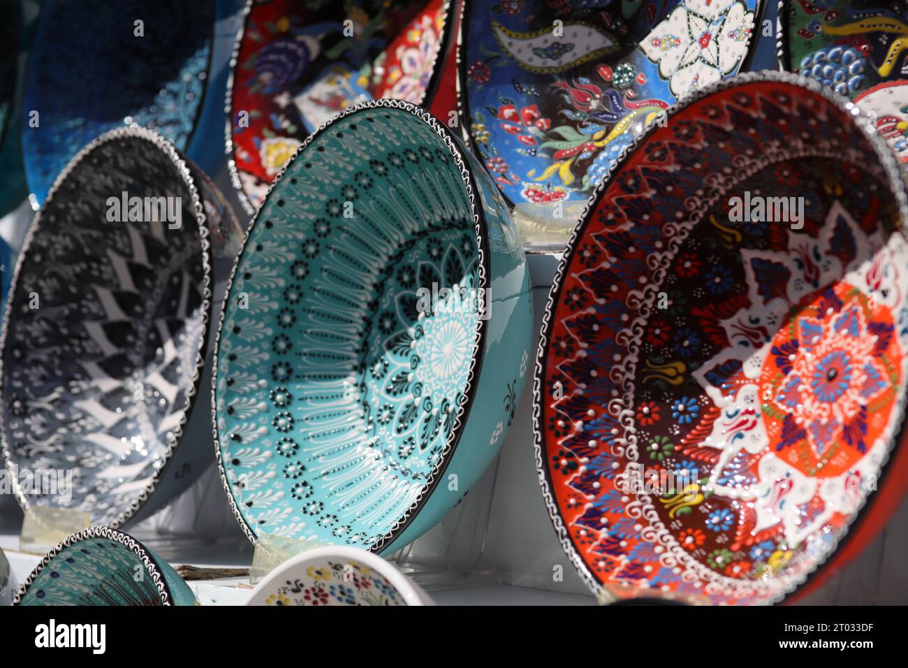 Reihen von wunderschönen, mehrfarbigen dekorativen Schalen mit verschiedenen Designs von sich wiederholenden und floralen Mustern, die auf weißen Regalen von der Seite aus gesehen ausgestellt sind Stockfoto