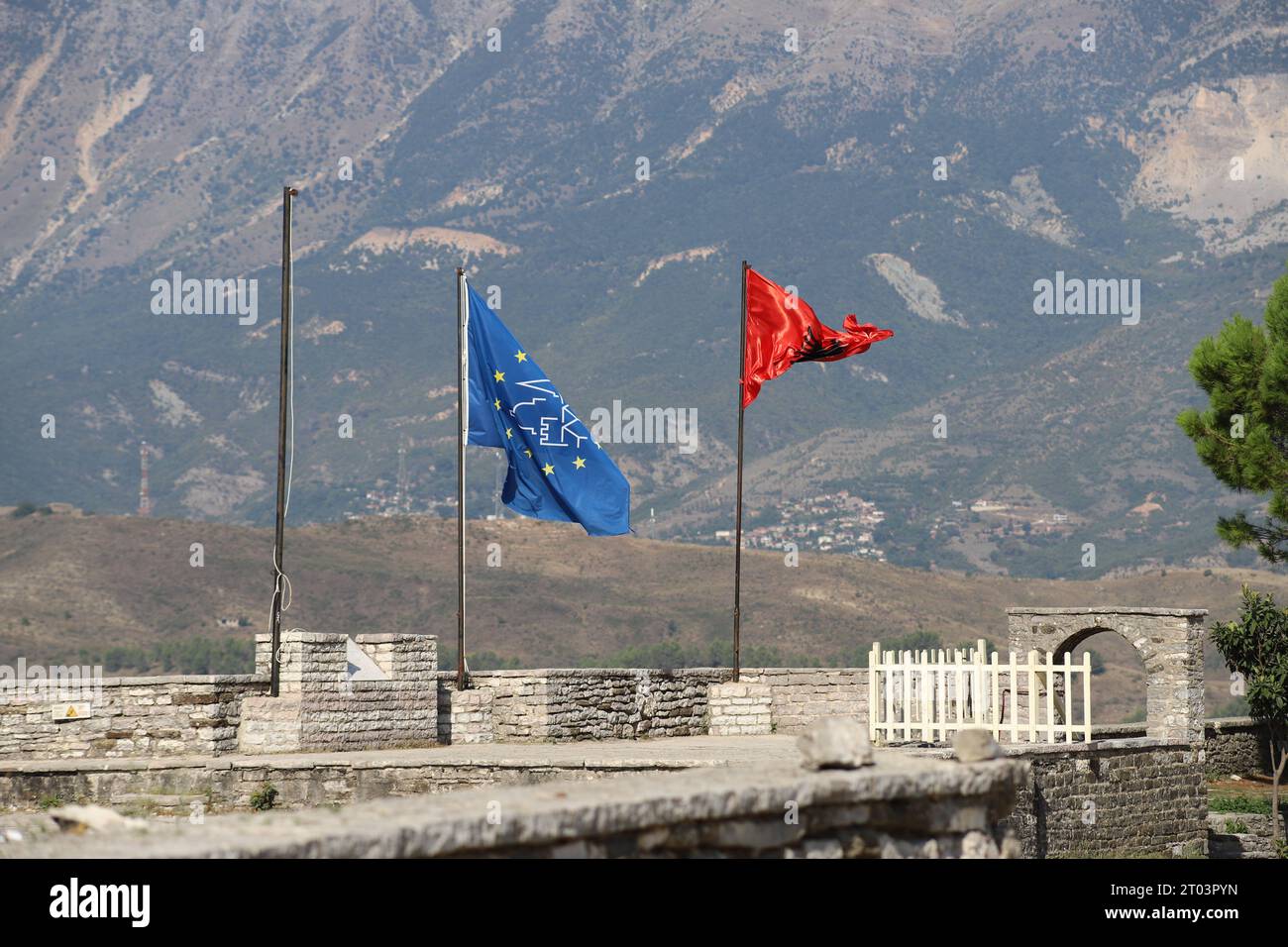 Eine blaue Flagge mit gelben Sternen und einem albanischen schwarzen Doppeladler auf rotem Hintergrund Besa, Fluss in der Brise mit Bergkulisse am Gjirokaster Castle Stockfoto