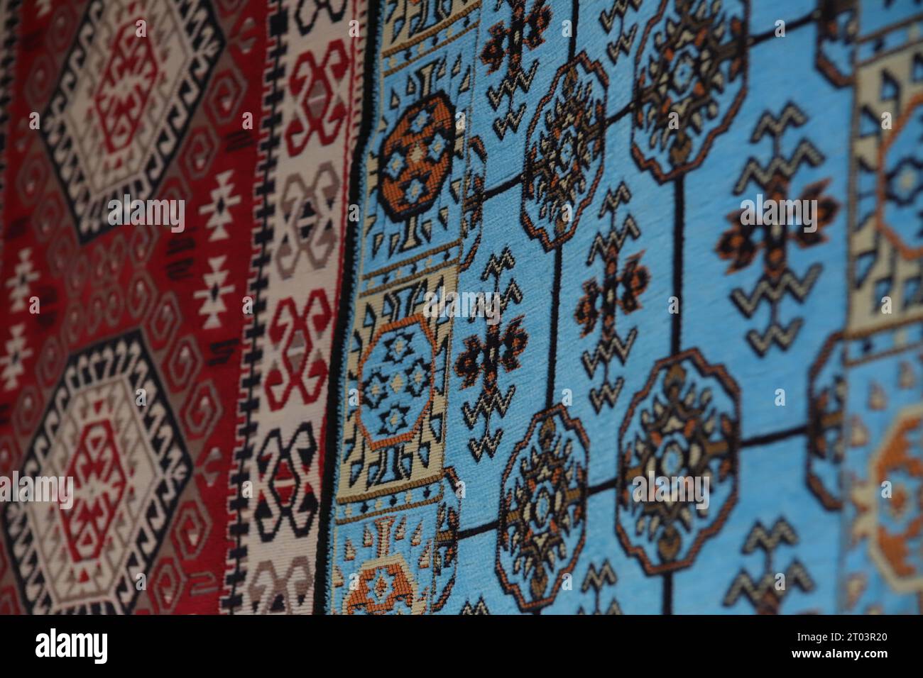Zwei wunderschöne, mit ethnischen Mustern versehene Teppiche, ein blauer und ein roter Teppich, hängen an einer Wand, die in den Straßen des Gjirokaster Baazar in Albanien ausgestellt wird. Stockfoto
