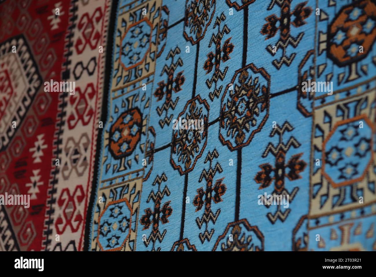 Zwei wunderschöne, mit ethnischen Mustern versehene Teppiche, ein blauer und ein roter Teppich, hängen an einer Wand, die in den Straßen des Gjirokaster Baazar in Albanien ausgestellt wird. Stockfoto
