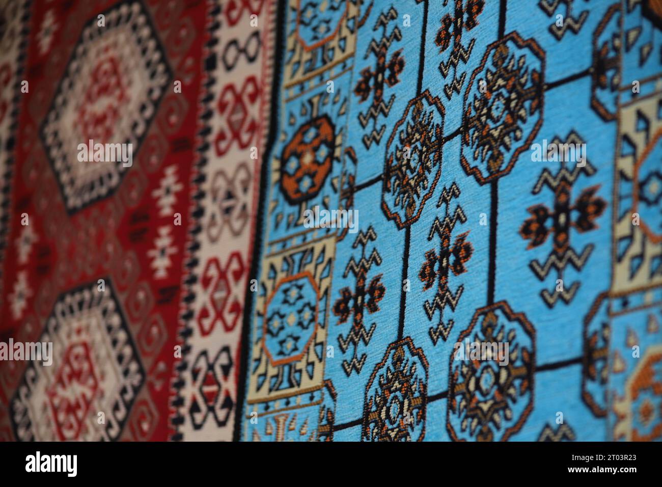 Zwei wunderschöne, mit ethnischen Mustern versehene Teppiche, ein blauer und ein roter Teppich, hängen an einer Wand, die in den Straßen des Gjirokaster Baazar in Albanien ausgestellt wird. Stockfoto