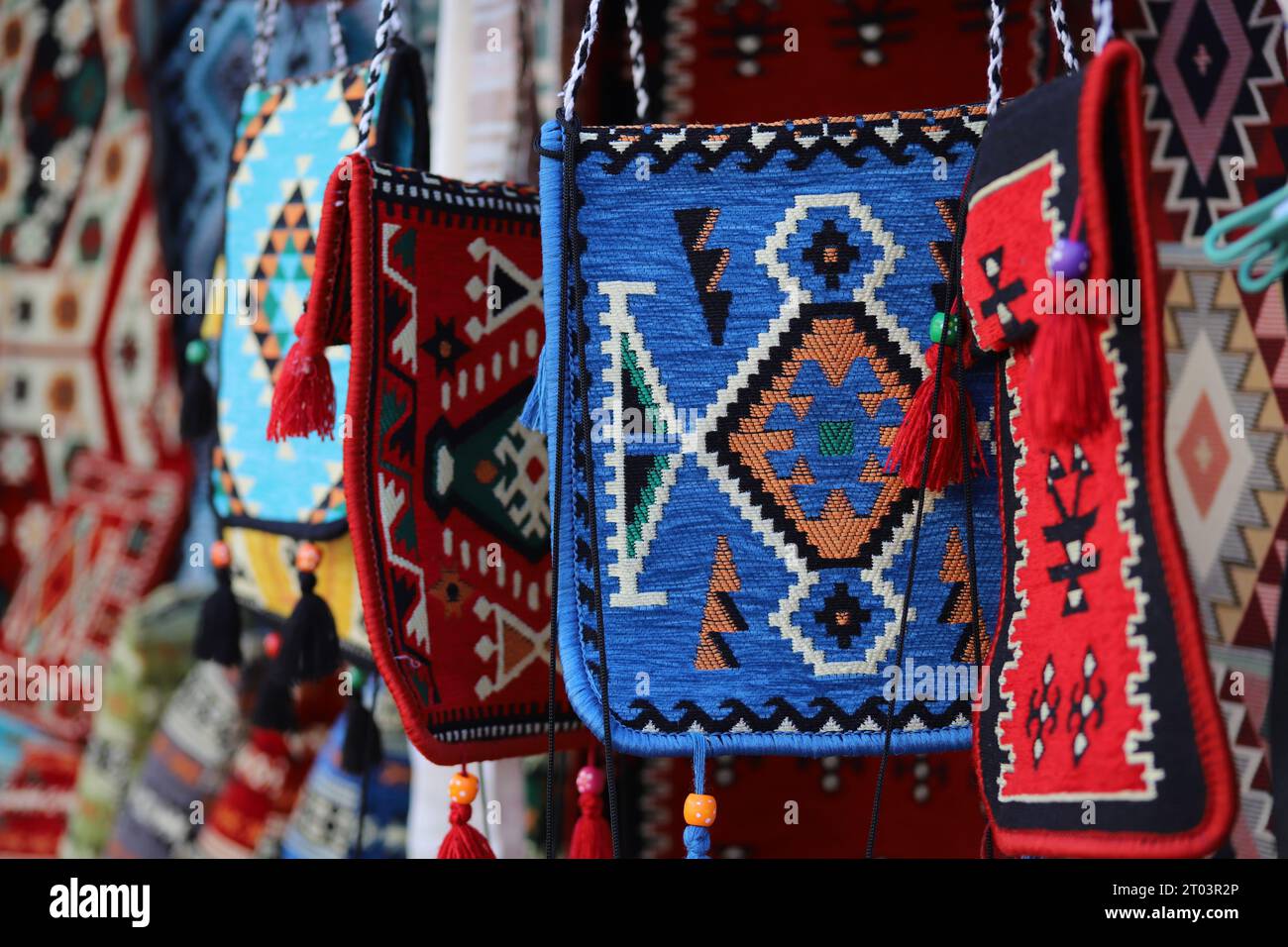 Eine ungleichmäßig hängende Reihe von auffälligen, geometrischen Mustern, mehrfarbigen, ethnischen Look, gewebten Teppich- oder Teppichschultertaschen mit Quasten und Perlen. Stockfoto