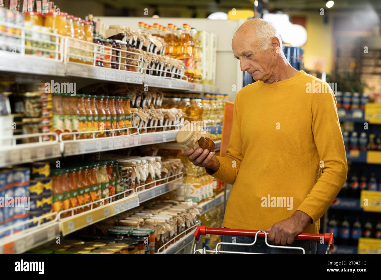 Älterer Mann im Supermarkt kaufte Lebensmittel mit einem Glas Salat, der im Supermarkt am Gang entlang ging Stockfoto