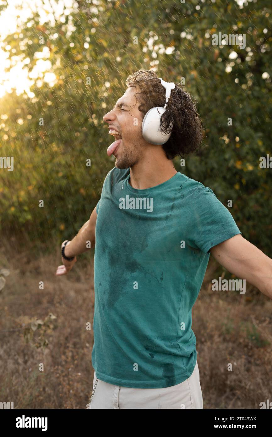 Arabischer junger Mann, der tanzt und Musik hört und den warmen Sommerregen genießt, drückt Freude aus Stockfoto