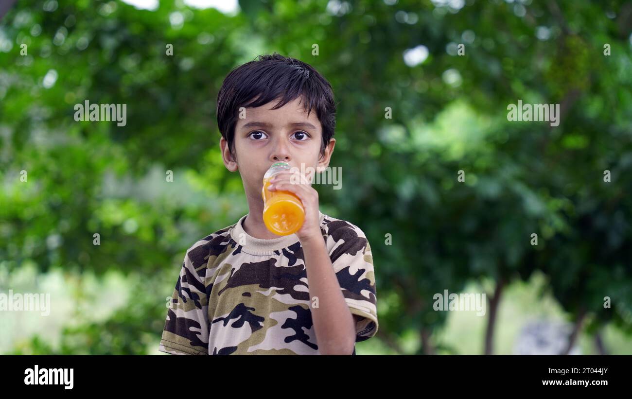 Junge trinkt Saft. Asiatisches Kind trinkt aus Plastikflasche. Porträt eines Jungen, der Orangensaft trinkt. Orangensaft in der Flasche. Menschen trinken Energy Drink Stockfoto