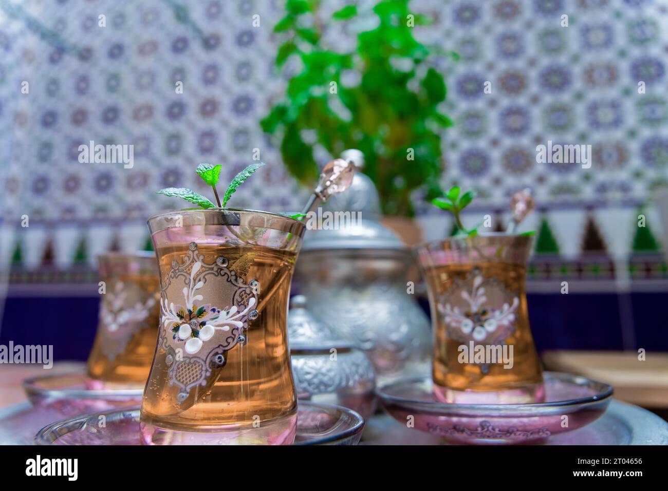 Maurischer Tee mit Minze, traditionelles marokkanisches Getränk in dekorierten Kristallgläsern, silberne Teekanne und Zuckerschale im Hintergrund Stockfoto