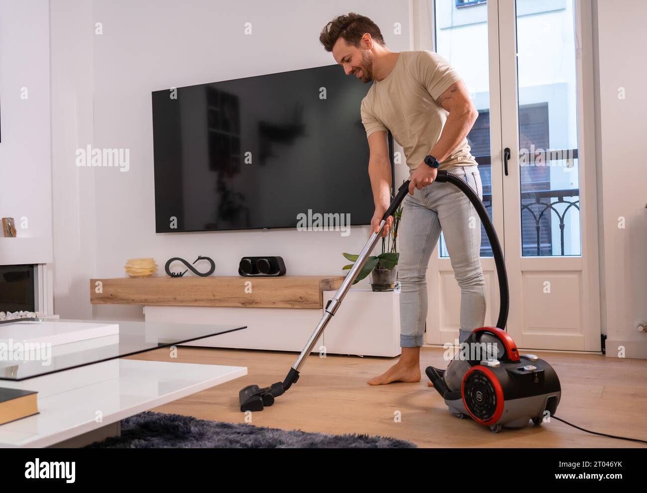 Ein Mann, der das Wohnzimmer im Haus mit einem Staubsauger reinigt Stockfoto