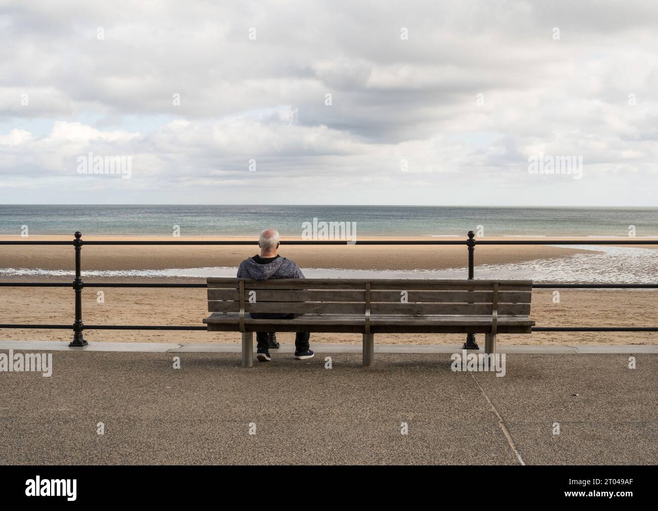 Ein älterer Mann sitzt allein mit Blick auf das Meer in Roker, Sunderland, England, Großbritannien Stockfoto