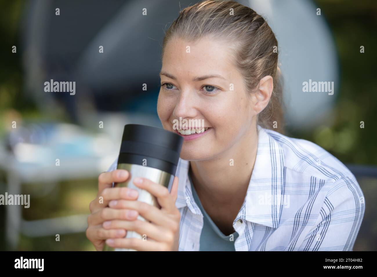 Frau genießt Kaffee aus einer isolierten Tasse beim Camping Stockfoto