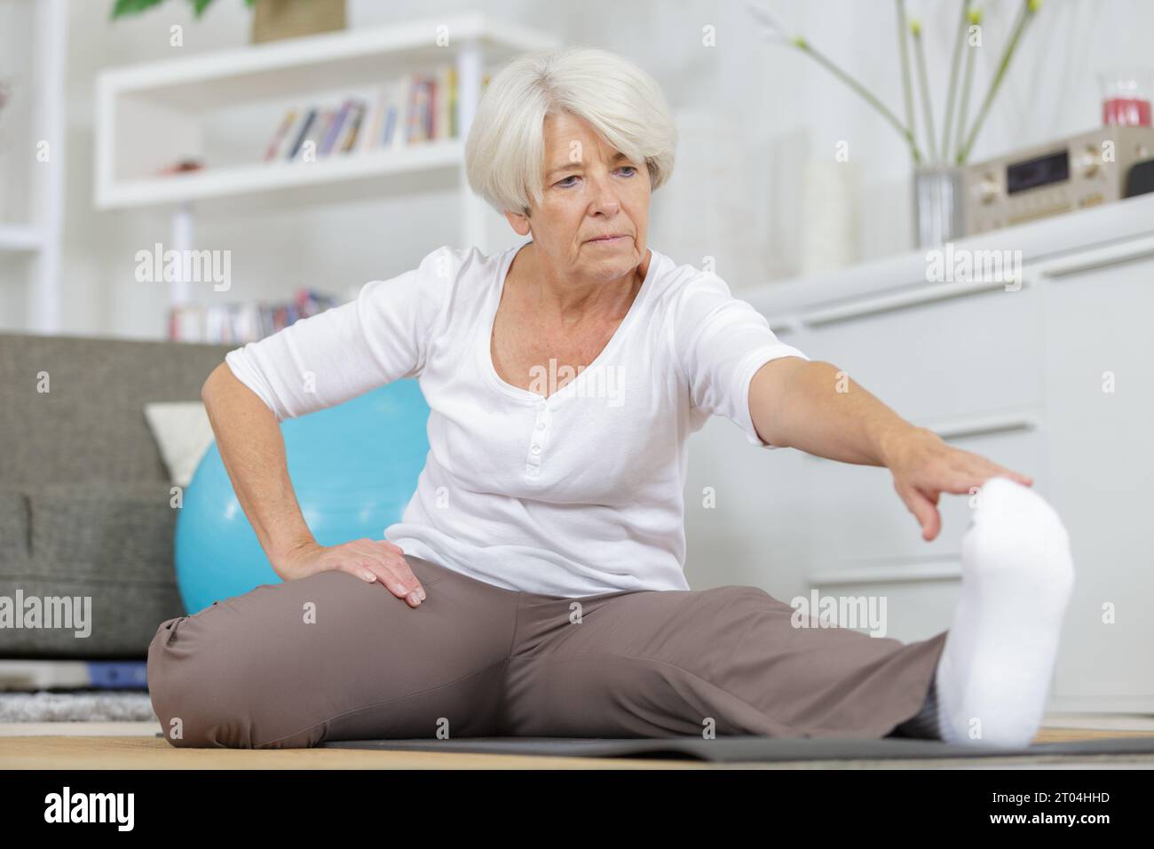 Glückliche Seniorin, die ihre Beine drinnen spannt Stockfoto