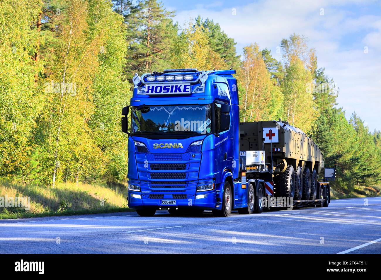 Der Blue Scania S500 Truck Hosike transportiert am Herbsttag ein militärisches Rettungsfahrzeug des Roten Kreuzes auf einem Tieflader-Anhänger. Raasepori, Finnland. September 2023. Stockfoto