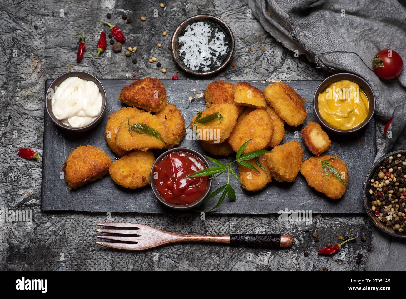Gebratene Hähnchenbrust - Nuggets auf einem Schneidebrett mit Soßen, Gewürzen und frischem Gemüse. Auf grauem Hintergrund Stockfoto