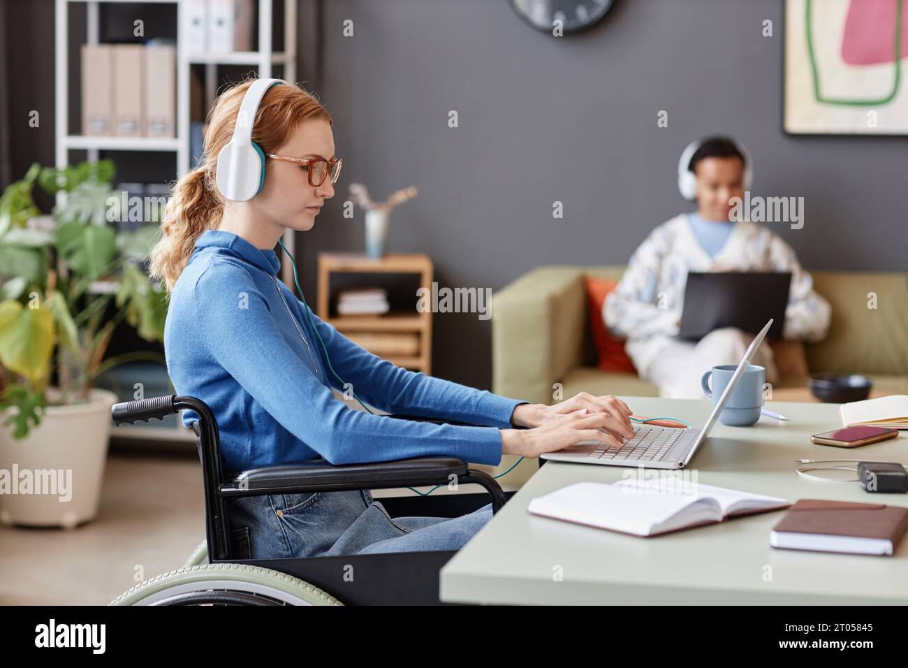 Seitenporträt einer jungen rothaarigen Frau mit Behinderung am Computer während der Arbeit in der IT-Firma, Kopierraum Stockfoto