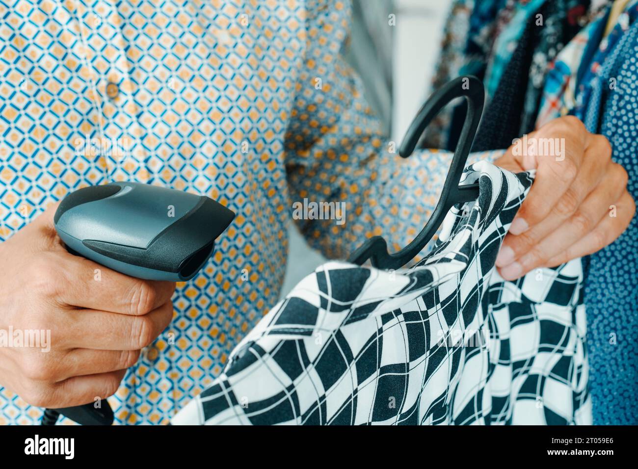 Nahaufnahme eines Verkäufers in einem Kleiderladen, der den Barcode eines schwarz-weißen Hemdes, das an einem Kleiderbügel hängt, mit einem Barcode-Scanner scannt Stockfoto