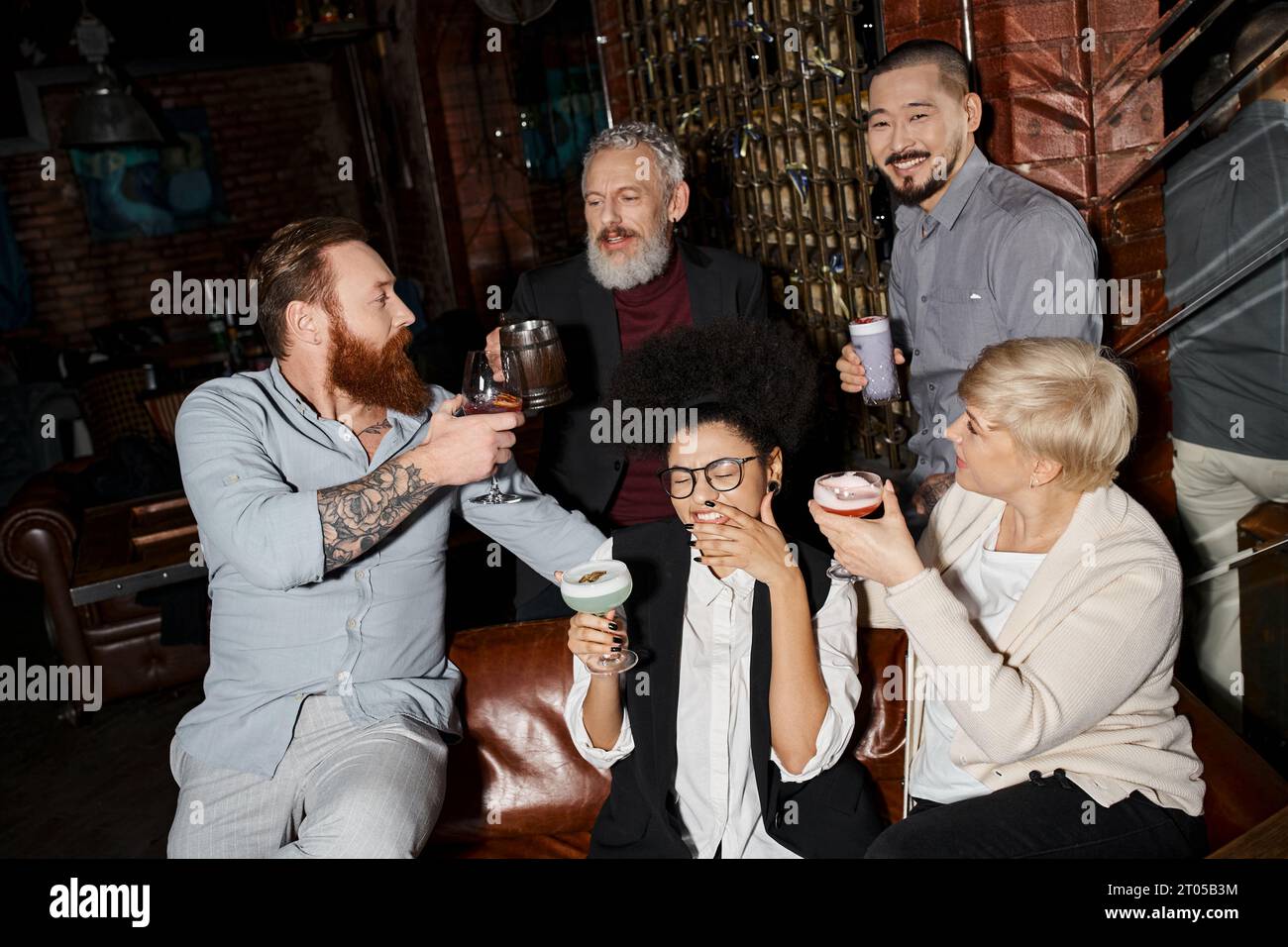 Freizeit multikultureller Kollegen, bärtige tätowierte Männer, die in der Bar neben fröhlichen Frauen tosten Stockfoto