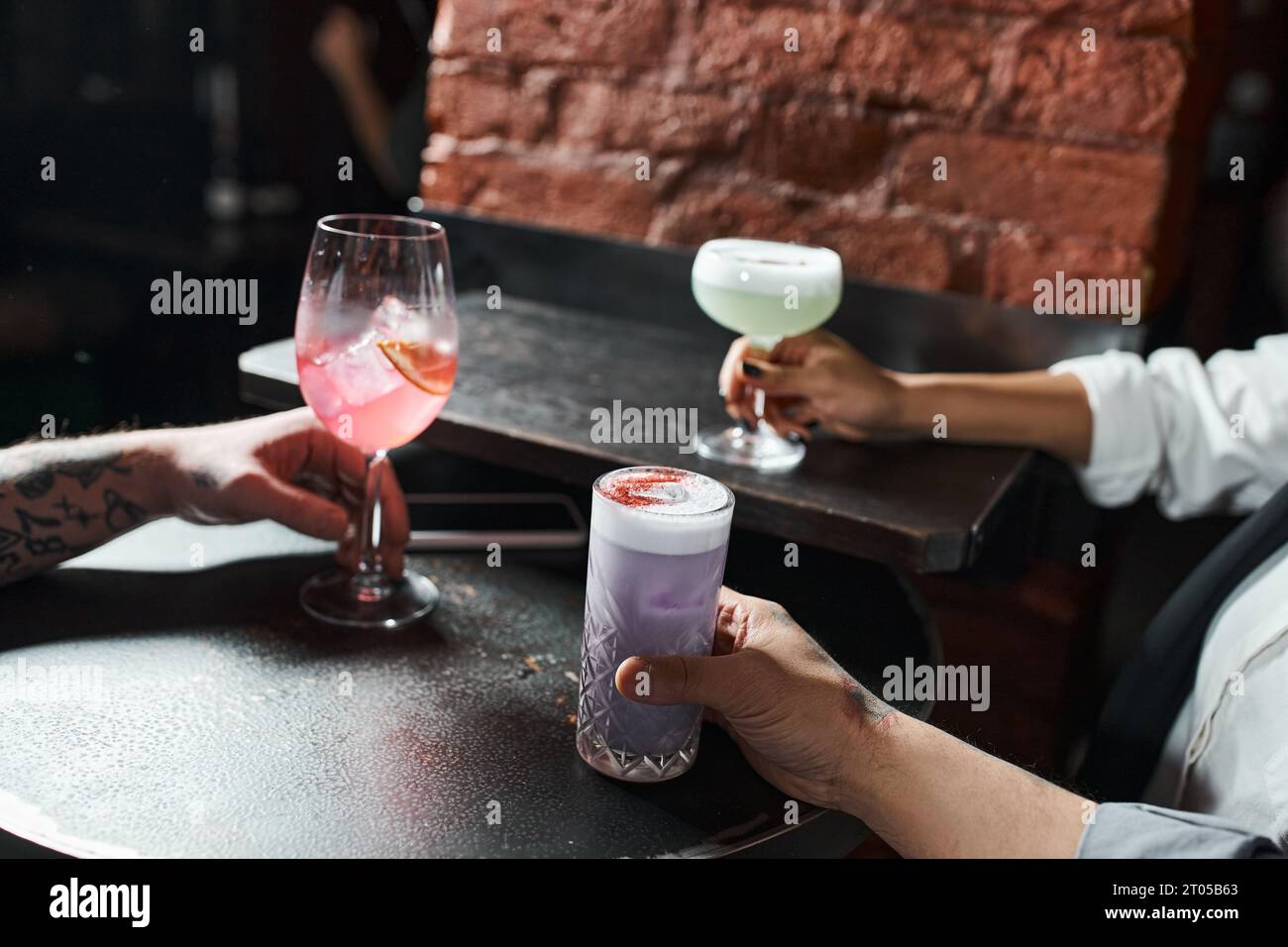 Zugeschnittene Ansicht von afroamerikanischen Frauen und tätowierten Männern mit Cocktails in der Bar, Freizeit nach der Arbeit Stockfoto