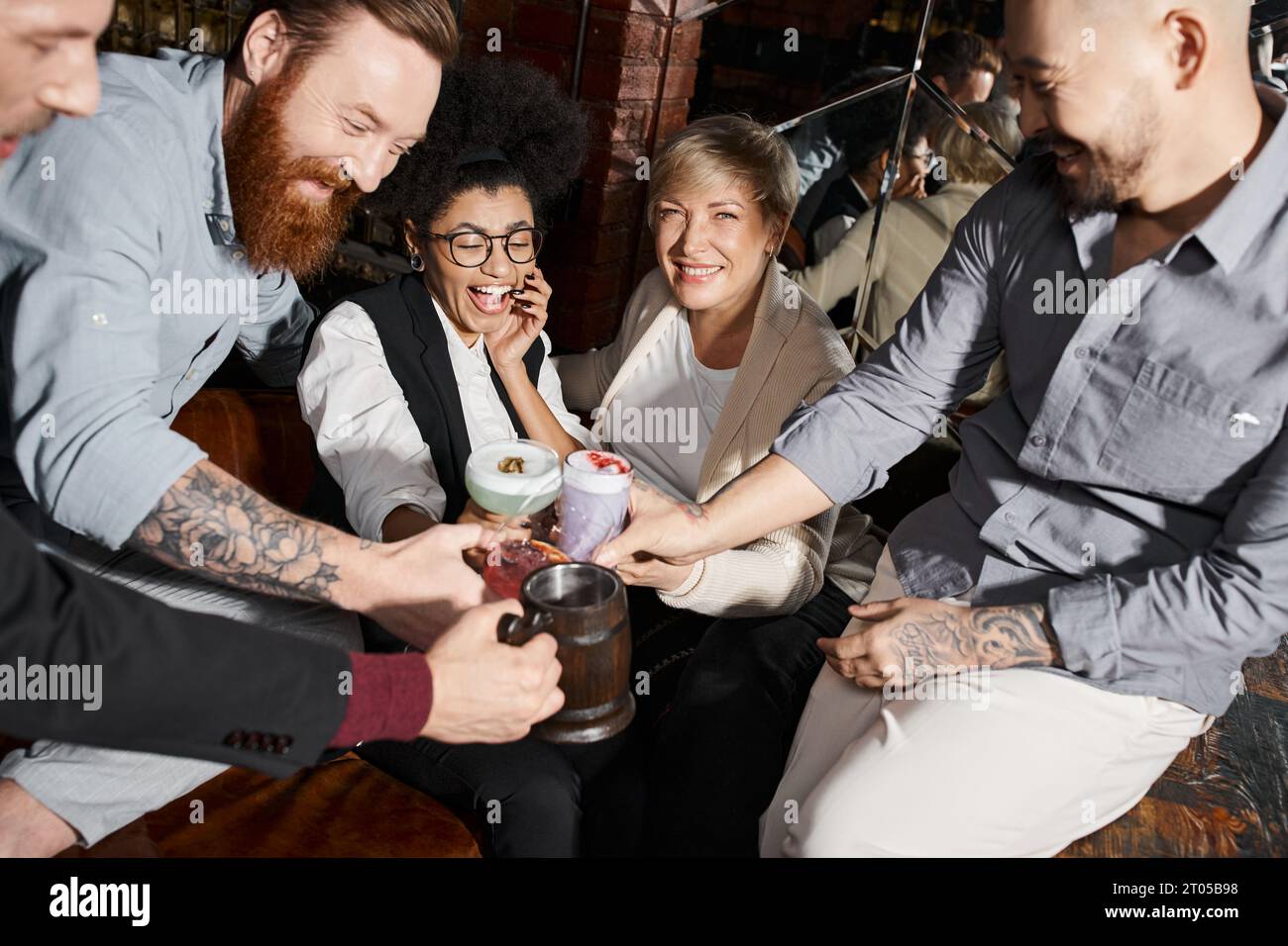 Glückliche Frauen und tätowierte Männer, die in der Bar Cocktails trinken, multiethnische Freunde haben Spaß Stockfoto