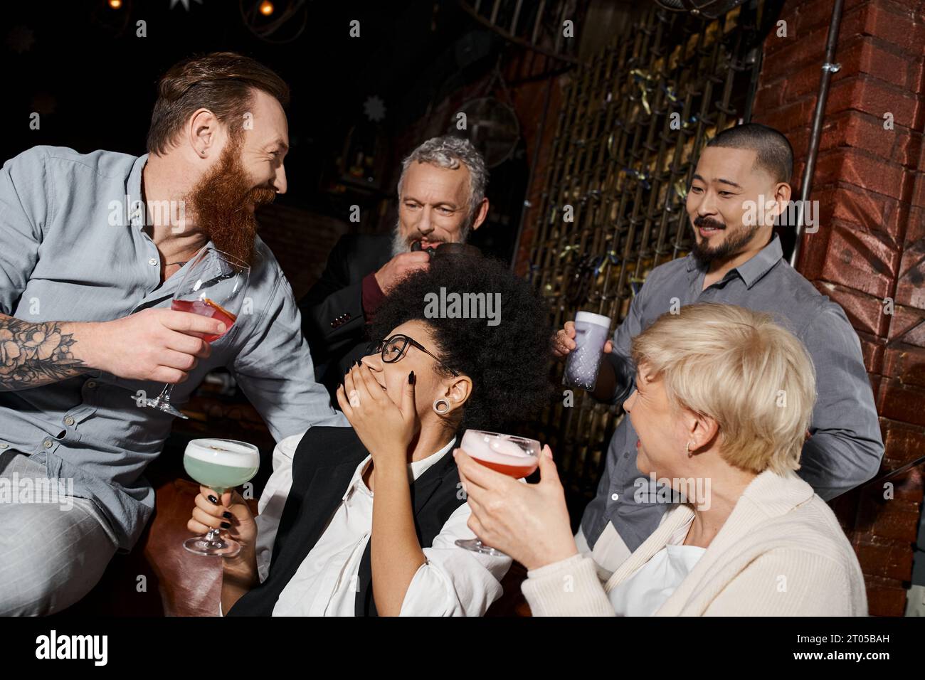 Tätowierte Männer und multiethnische Frauen mit Cocktails in der Bar, glückliche Kollegen auf Drinks Stockfoto