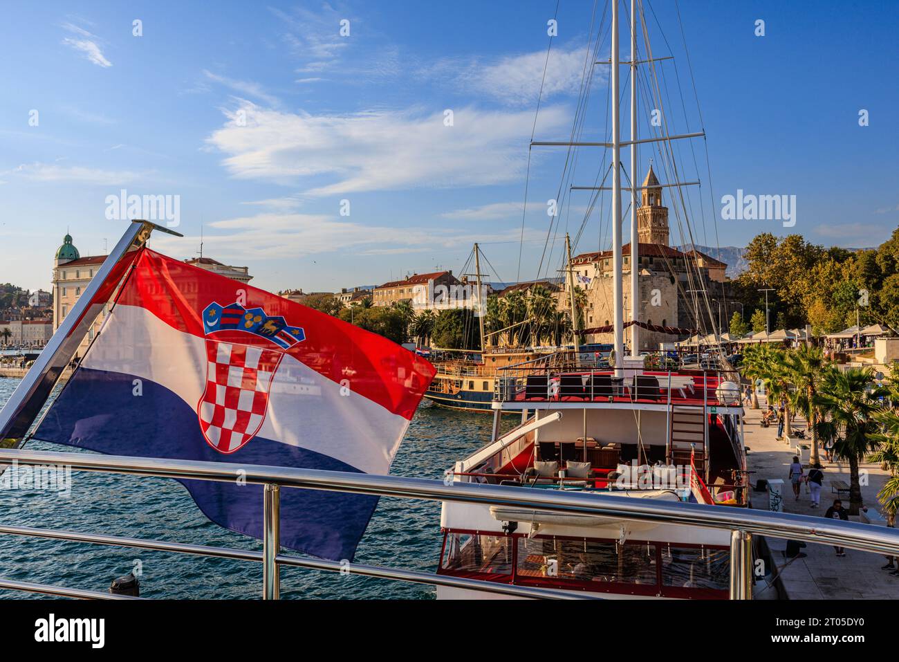 Die kroatische Flagge fliegt im Wind am Heck eines kleinen Kreuzfahrtschiffes, das am baumgesäumten Hafen vor dem historischen Zentrum von Split liegt Stockfoto