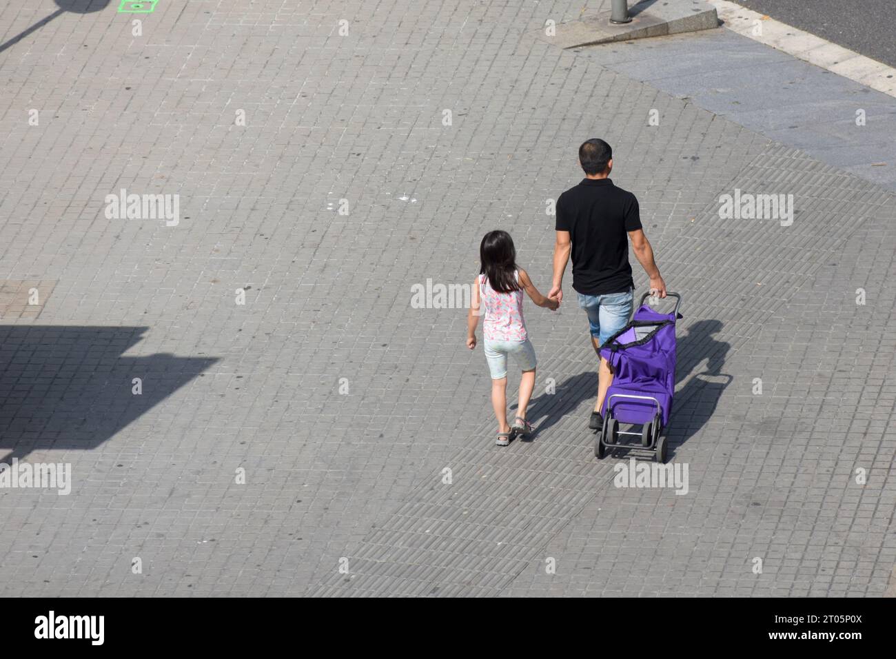 Rückansicht eines Vaters und seiner Tochter, die mit einem Einkaufswagen die Straße hinunter gehen. Stockfoto