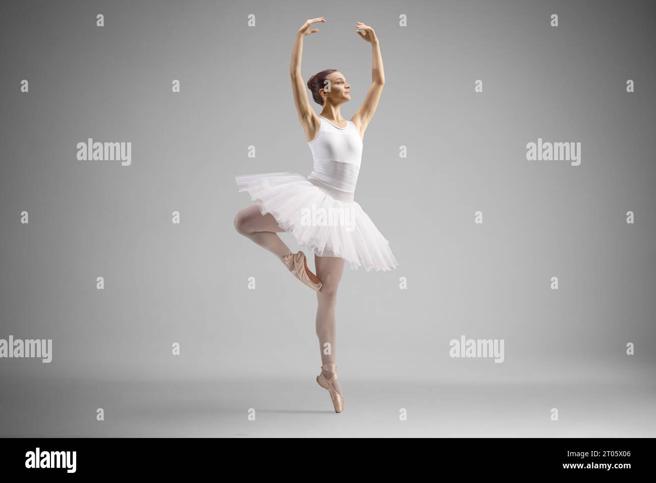 Aufnahme einer Ballerina in einem weißen Kleid, die isoliert auf grauem Hintergrund tanzt Stockfoto