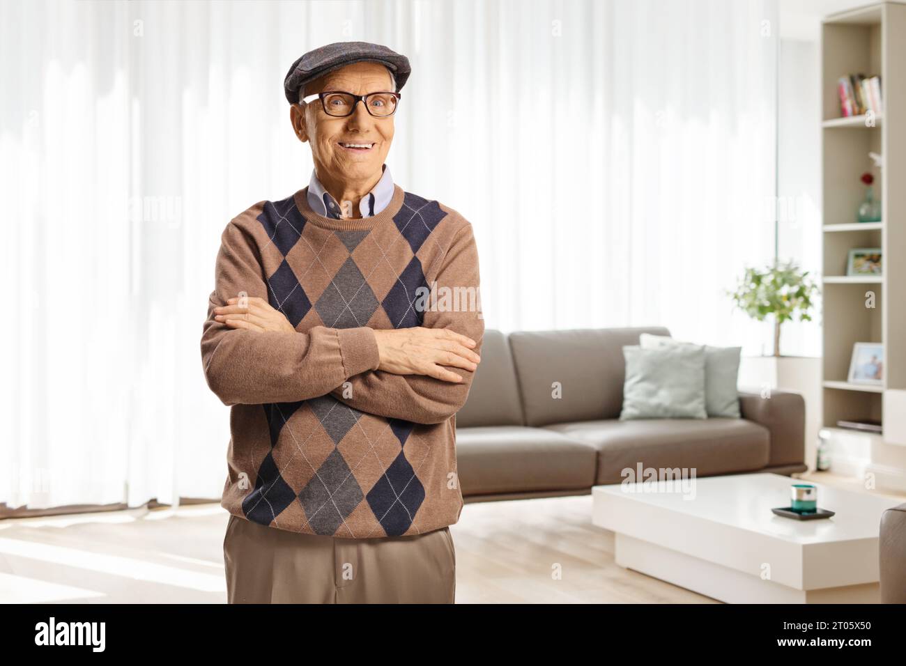 Fröhlicher älterer Mann posiert mit gefalteten Armen zu Hause in einem Wohnzimmer Stockfoto