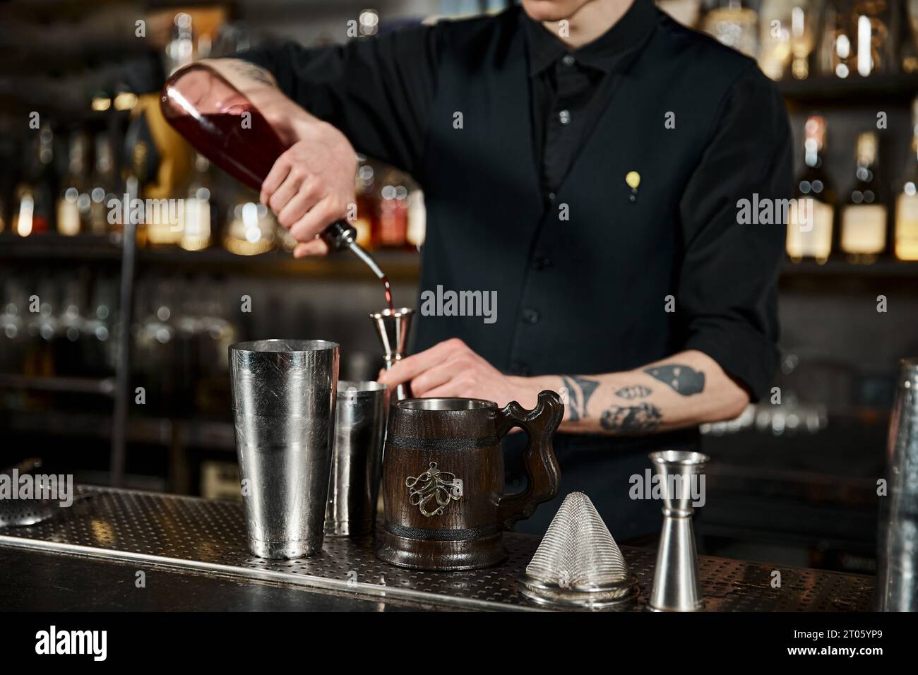 Zugeschnittene Ansicht des Bartended, der Alkohol in das Jigger in der Nähe eines Holzbechers gießt, Cocktailkünstlerin Stockfoto