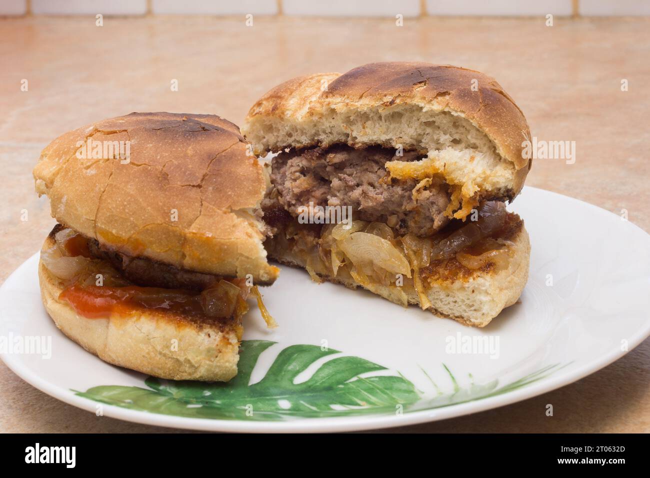 Eine Nahaufnahme eines geteilten Hamburger auf einem weißen Teller, serviert mit geröstetem rustikalem Brot, auf einer rustikalen Holzarbeitsfläche. Essen und Fleisch. Stockfoto