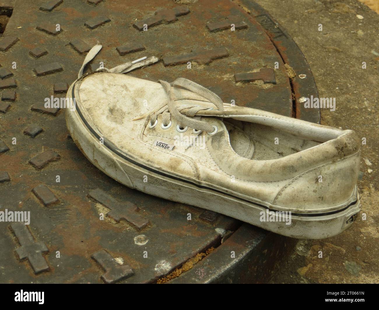 Nahaufnahme eines weißen Vans-Schuhs auf einem Kanalgitter Stockfoto
