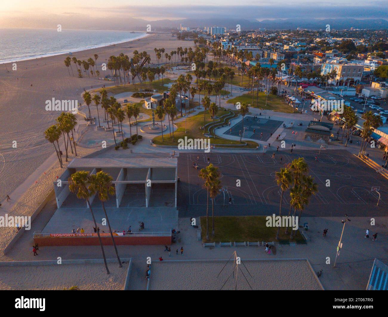 Luftaufnahmen mit einer Drohne während eines Winteruntergangs in Venice Beach, Los Angeles, Kalifornien, auf die Basketballfelder, Palmen und kurvige lan Stockfoto