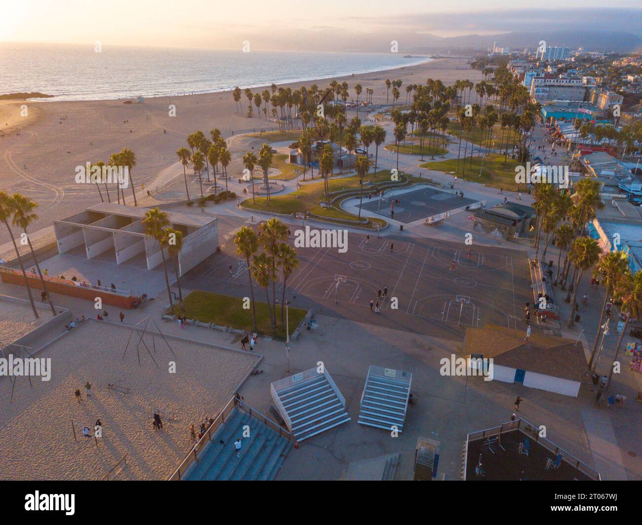 Luftaufnahmen mit einer Drohne während eines Winteruntergangs in Venice Beach, Los Angeles, Kalifornien, auf die Basketballfelder, Palmen und kurvige lan Stockfoto