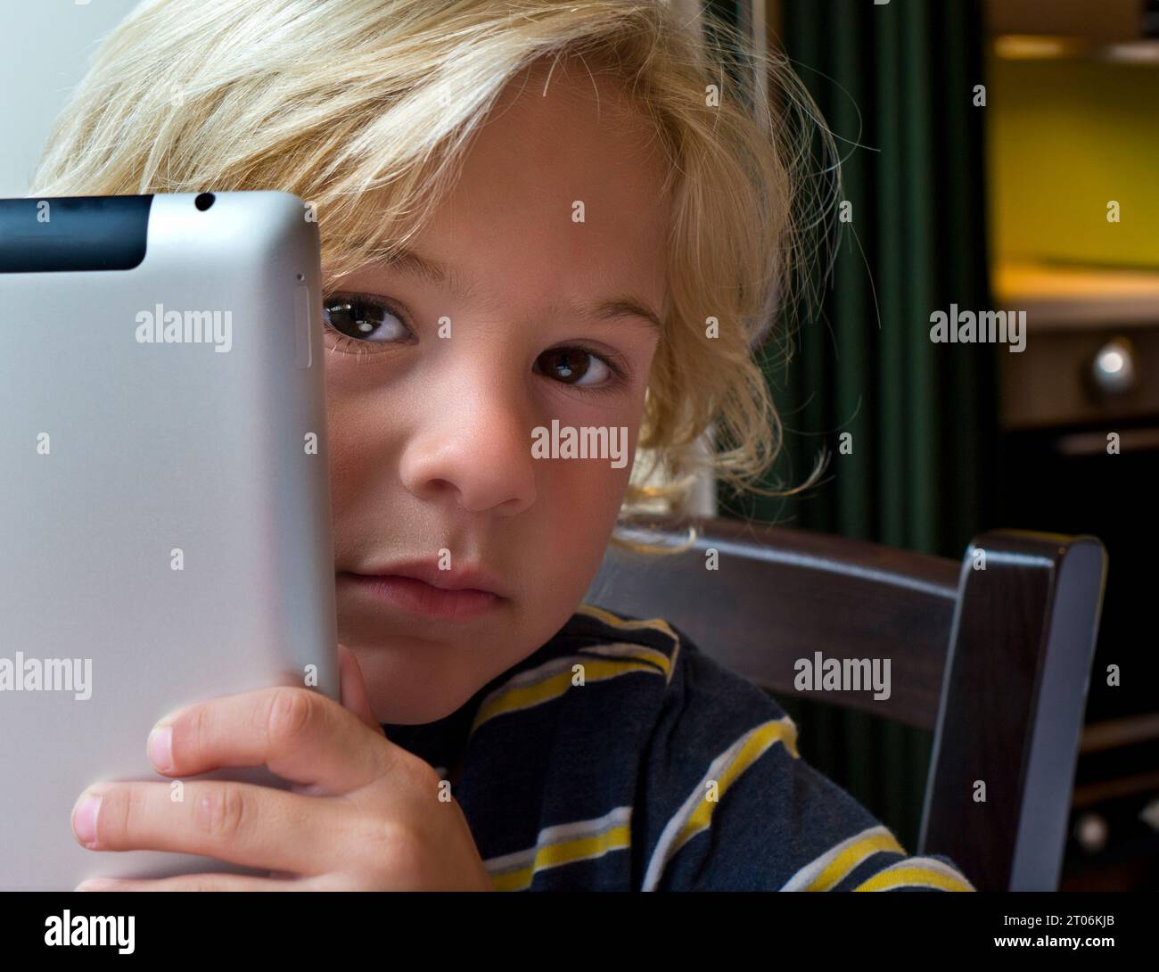 Junge 5-7 Jahre blonde Junge mit Tablet-Computer mit nachdenklichem Ausdruck, der geheimnisvoll auf die Bildschirminformationen auf seinem Tablet iPad-Computer blickt Stockfoto